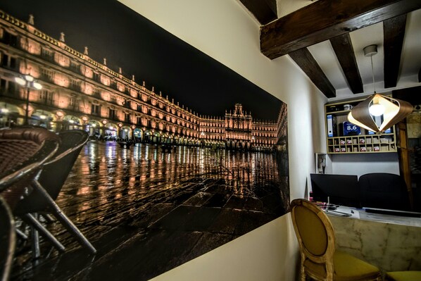 Una habitación con un amplio mural de un edificio histórico, techo de madera y un escritorio con lámpara.