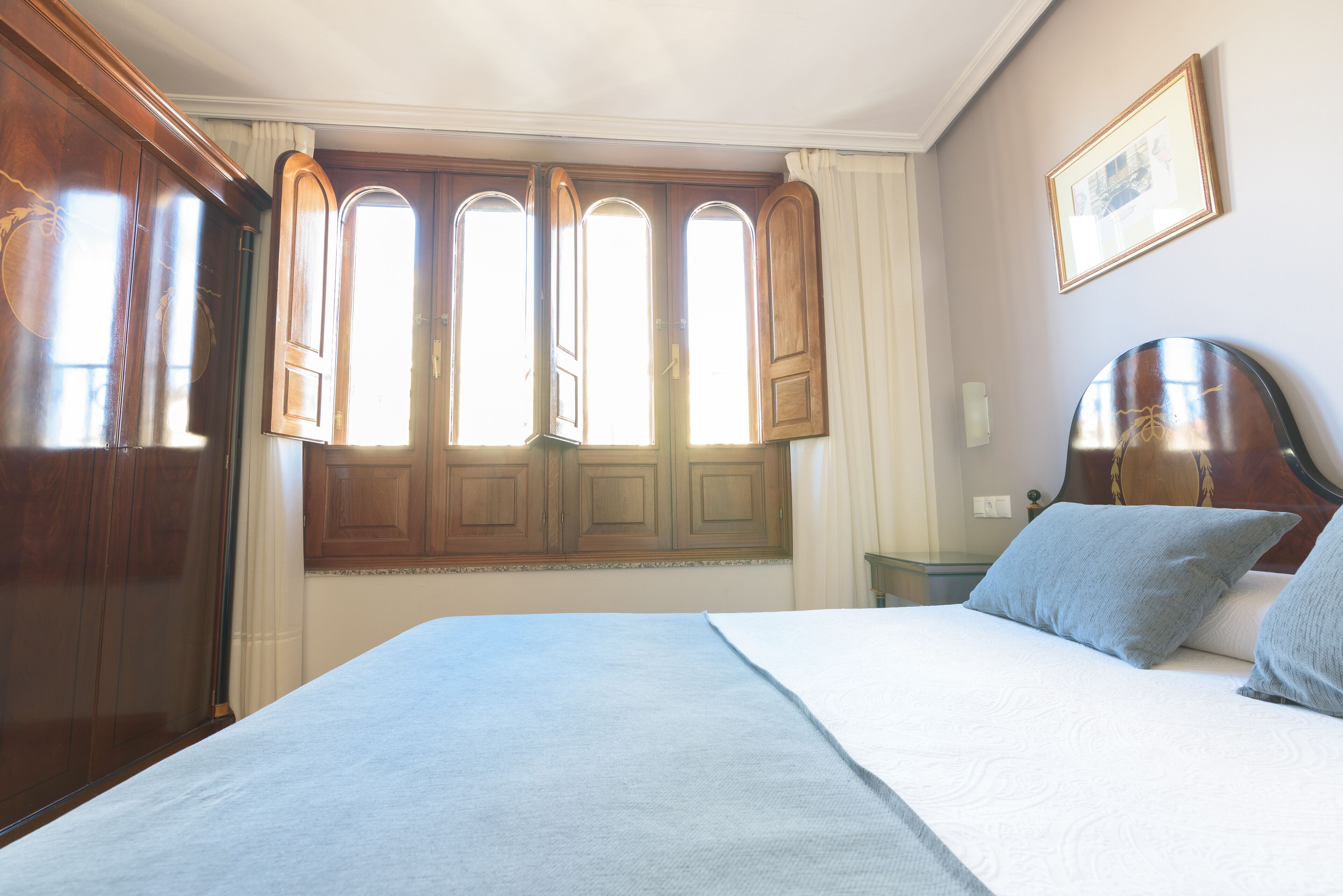 A bedroom with a large bed, wooden wardrobe, and a window with curtains.