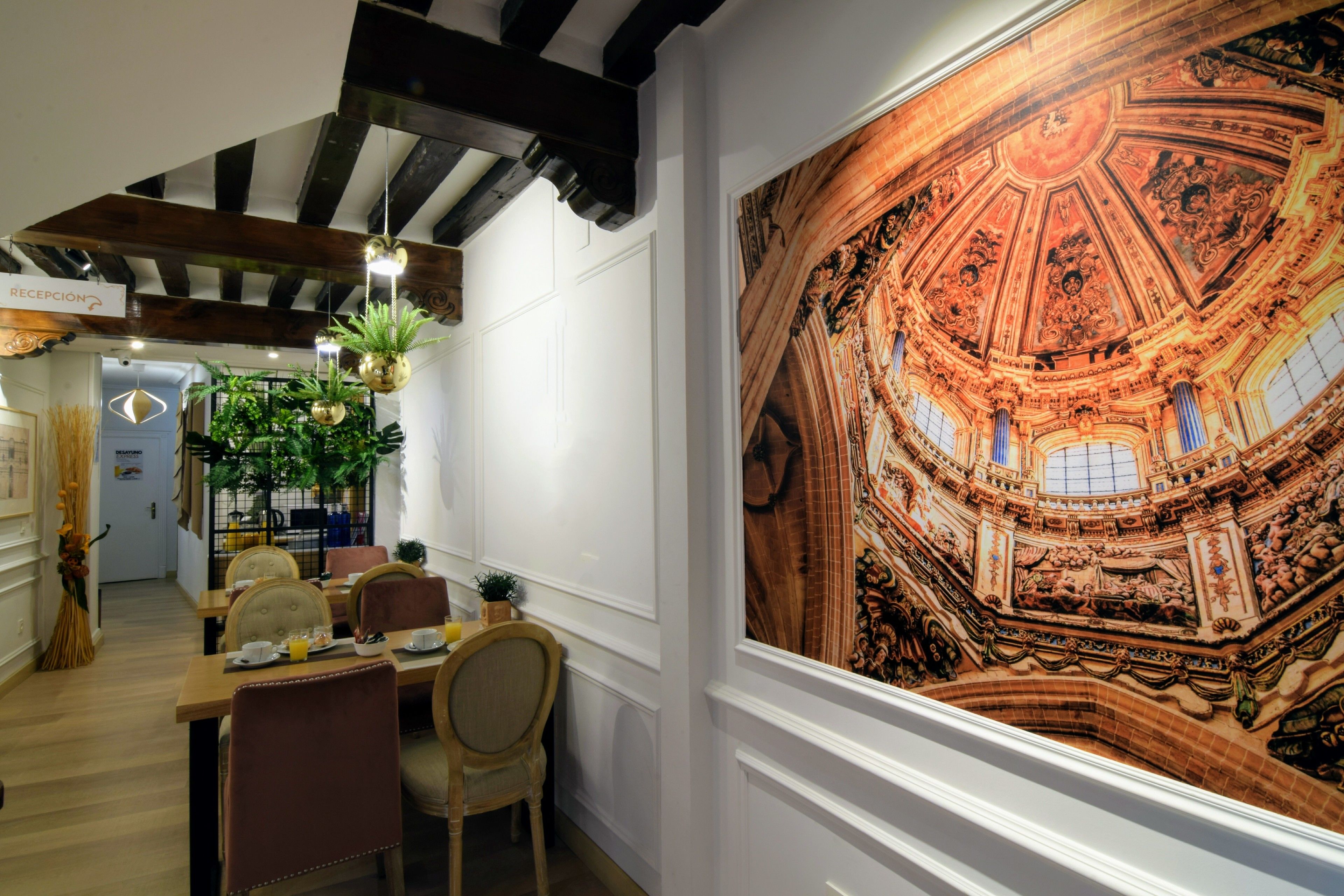 A dining area with a large mural of a grand architectural ceiling, wooden beams, and a reception desk.