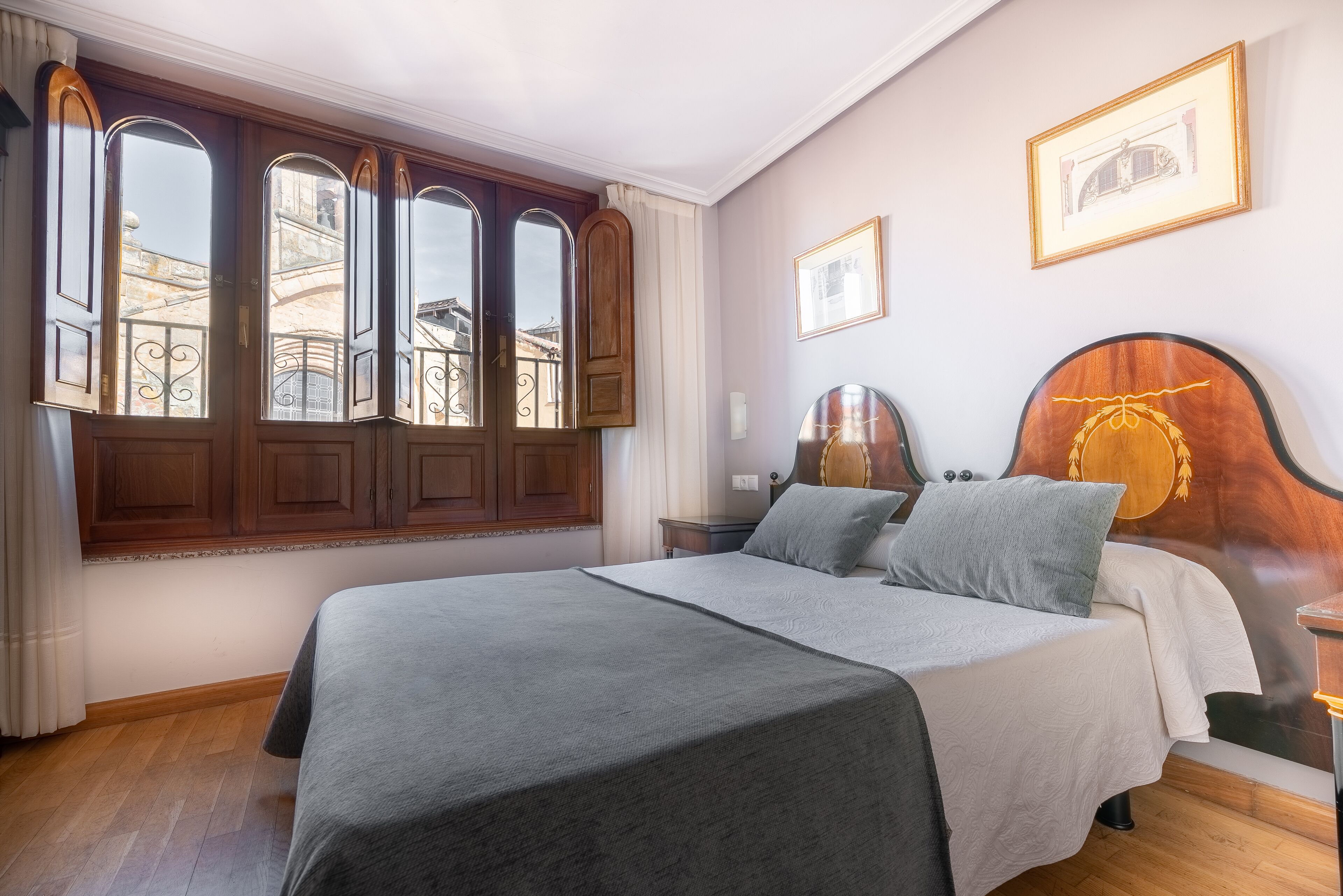 A bedroom with a large bed, wooden headboard, and a window with curtains.