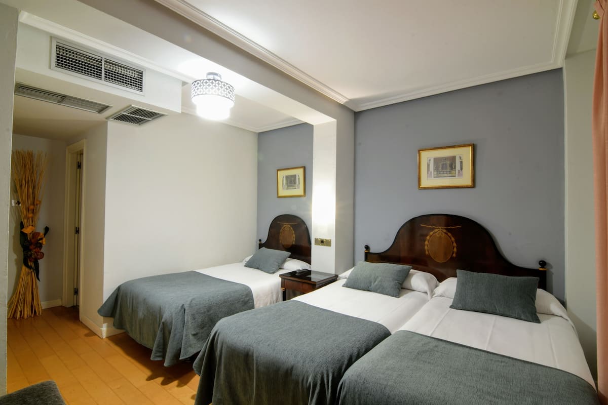 A hotel room with two single beds, a wooden headboard, a bedside table, and a wall-mounted picture.