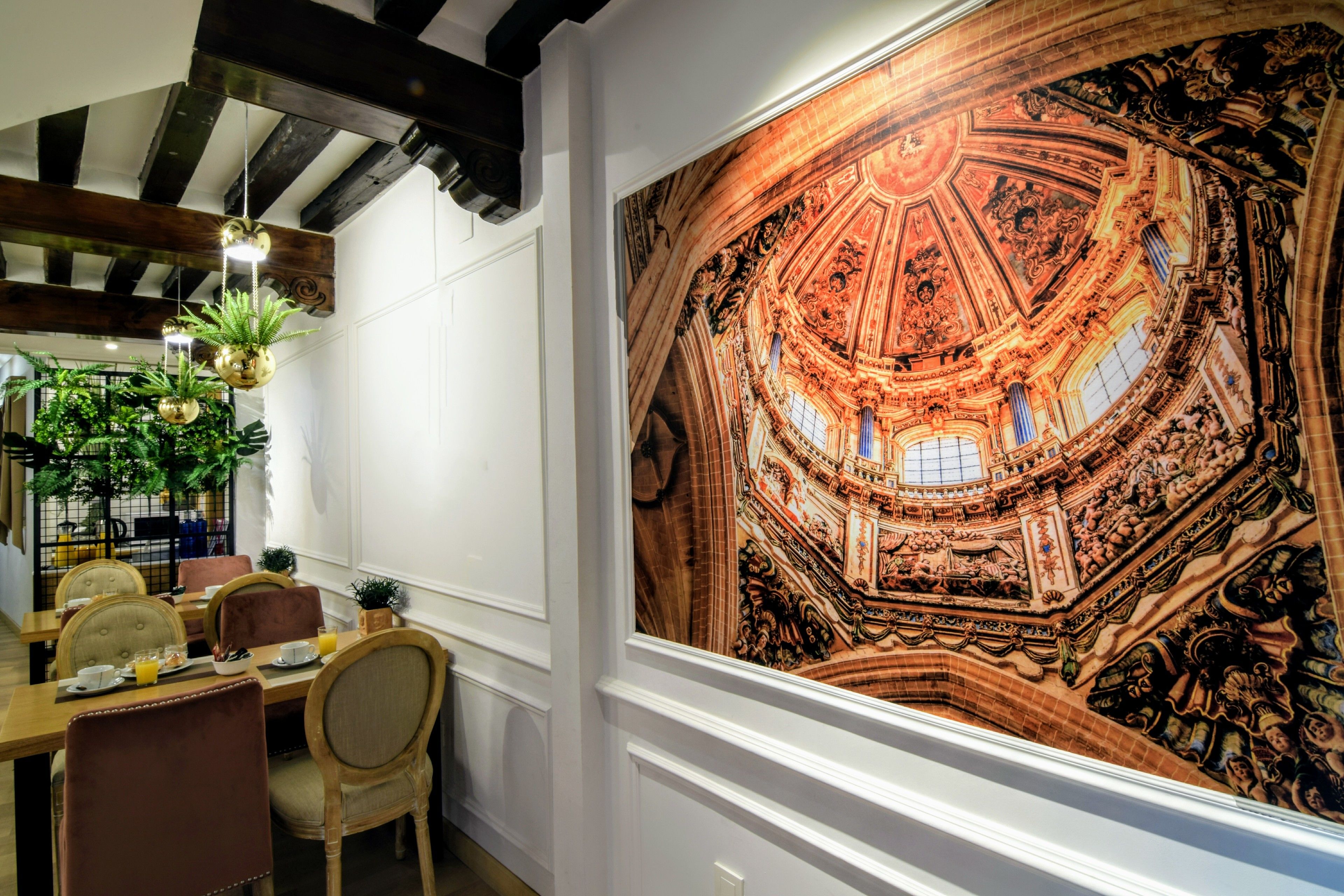 Un comedor con un gran mural de un techo histórico, vigas de madera y mobiliario moderno.