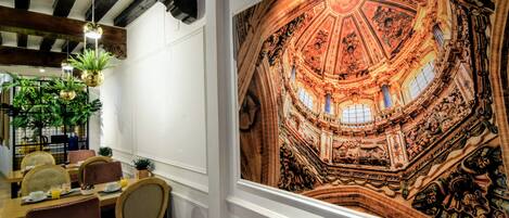 Un comedor con un gran mural de un techo histórico, vigas de madera y mobiliario moderno.