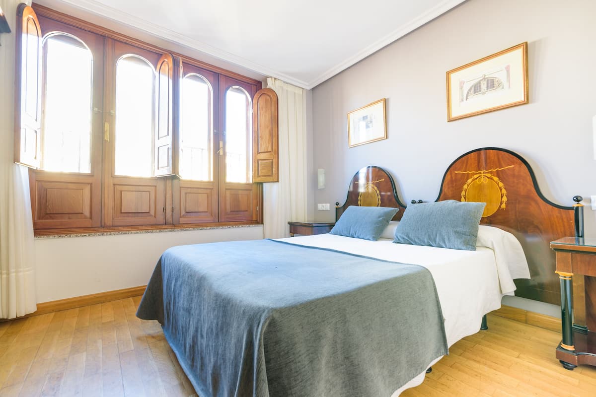 A bedroom with a large bed, wooden wardrobe, and a window with curtains.