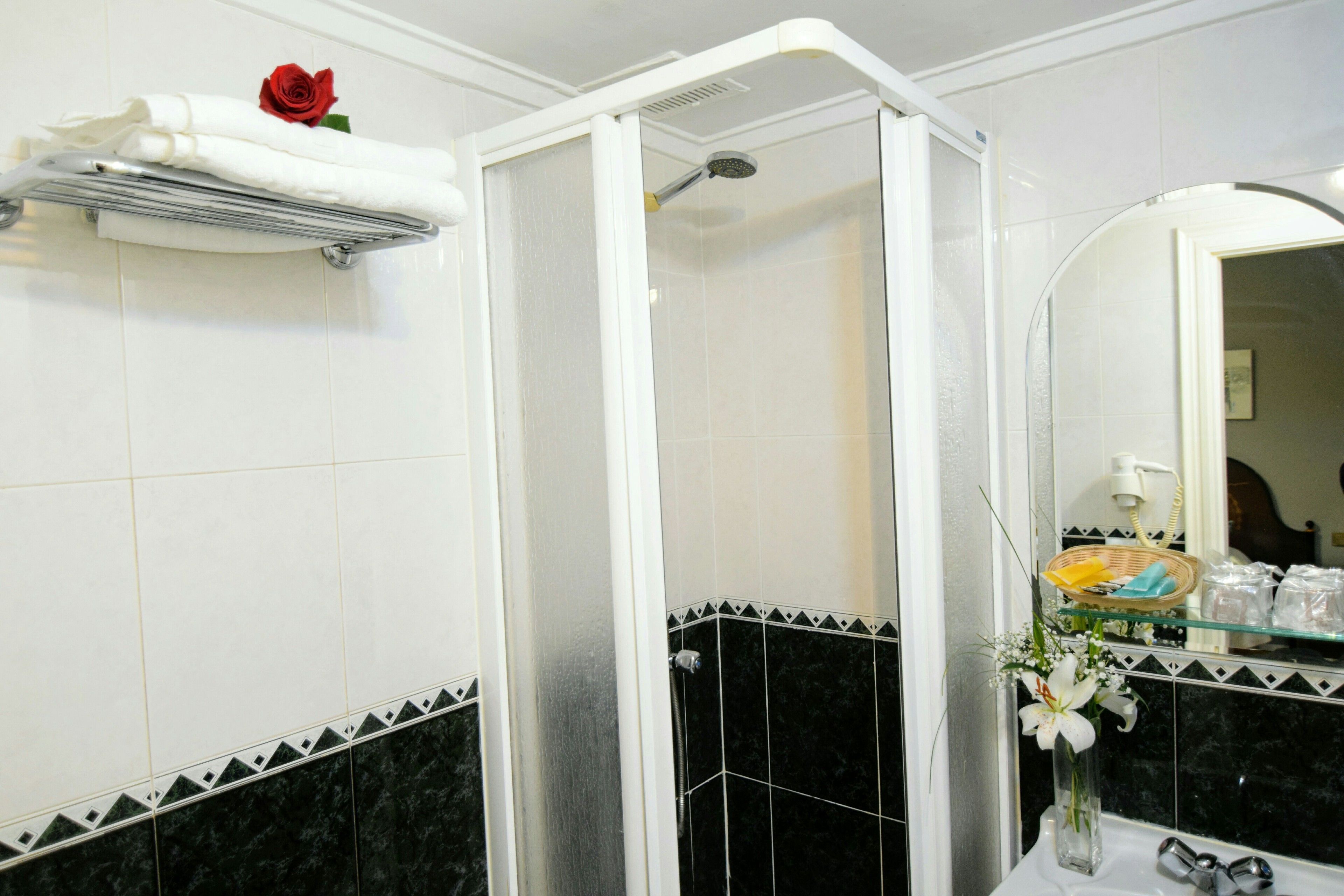 A bathroom with a shower enclosure, a towel rack with a rose, and a vase with flowers on the counter.