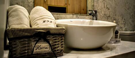 A bathroom with a marble countertop, a white sink, and a wicker basket labeled "Home" containing two towels.