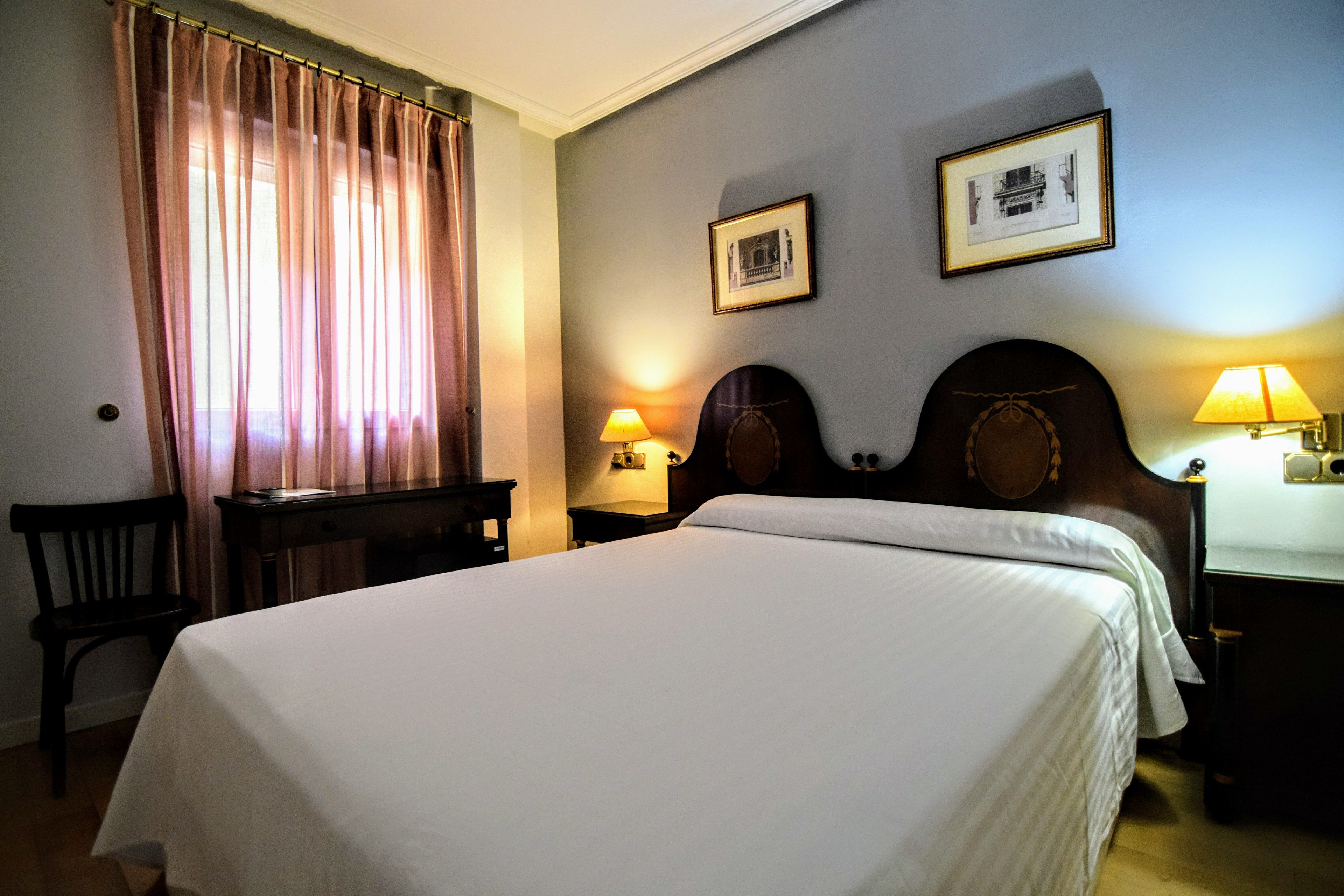 A hotel room with a large bed, a desk, two lamps, and a chair.