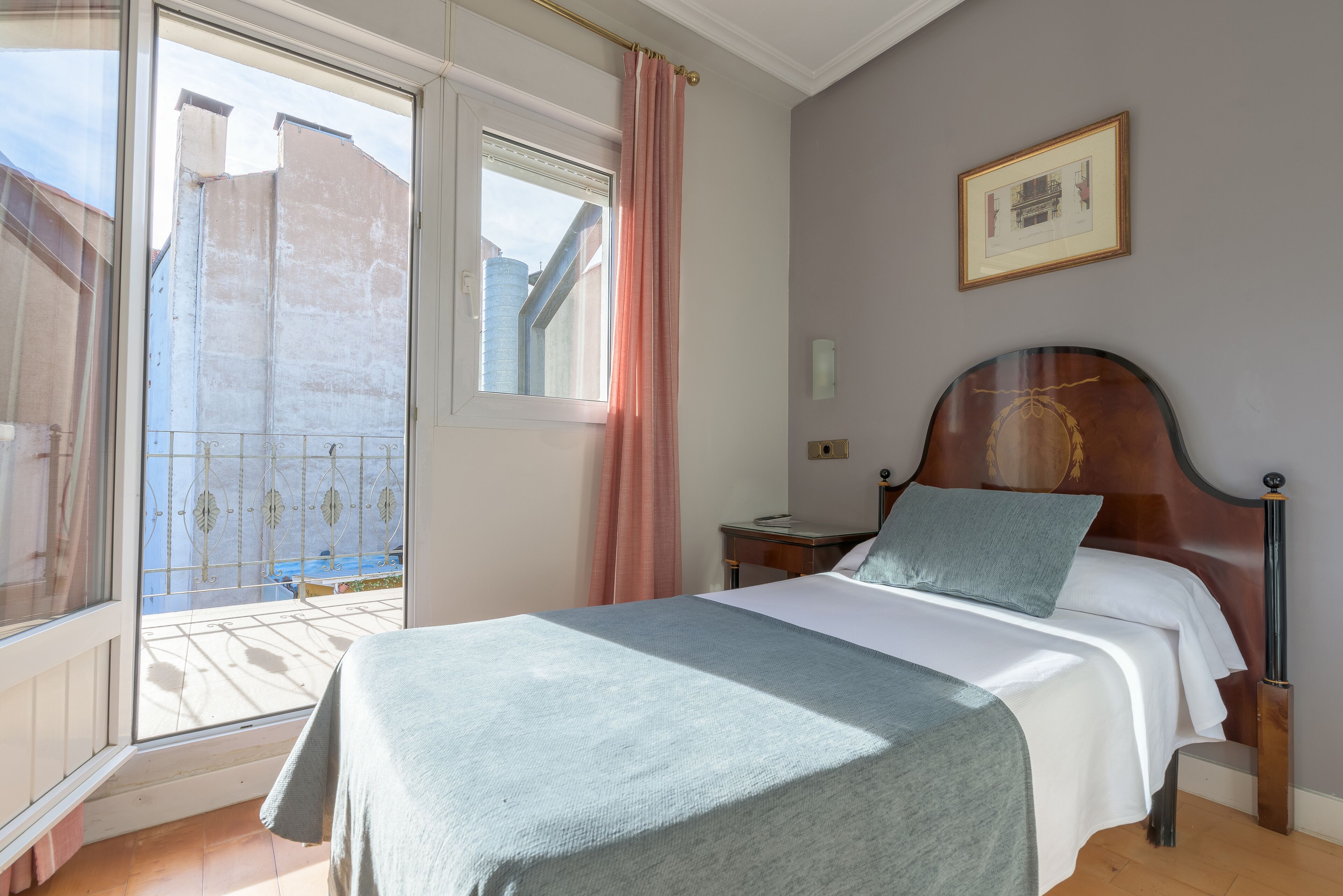 A bedroom with a bed, a nightstand, a framed picture on the wall, and a window with a curtain.