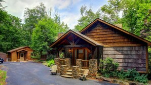 Un chalet rustique doté d’un porche en pierre et d’une façade en bois, entouré d’une végétation luxuriante.