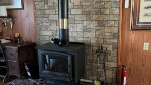 A wood-burning stove with a chimney, a stone wall, and a framed picture on the wall. - The Charter House formally known as The Charter Room. A 3 bedroom house for rent (Ocracoke)