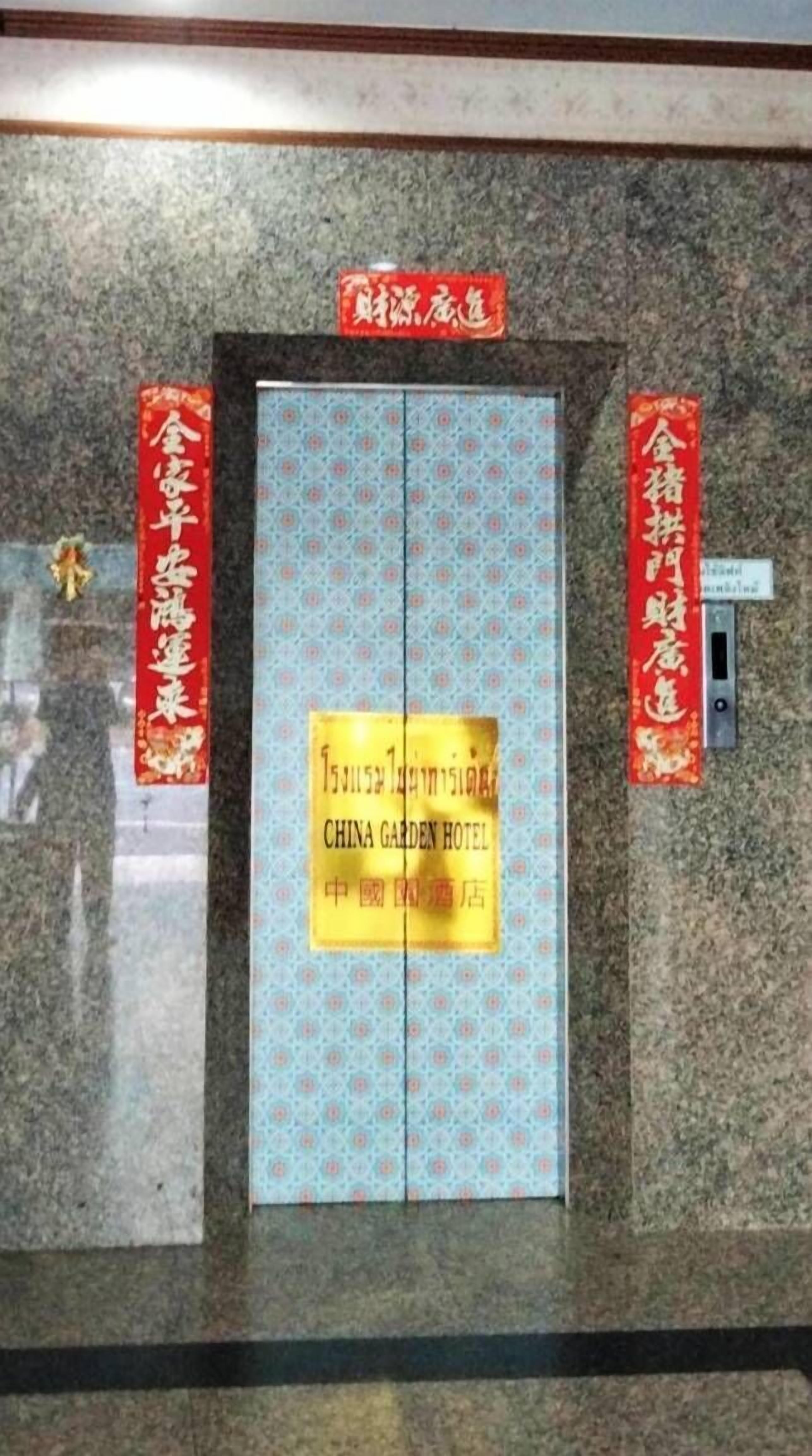 Ascensor del China Garden Hotel con una puerta ornamentada y pañoletas rojas a cada lado.