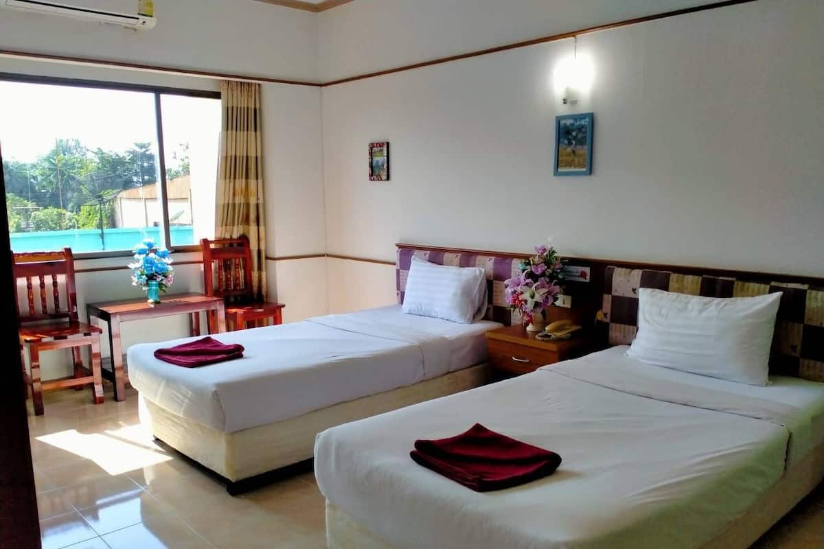 Une chambre d’hôtel avec deux lits, une petite table, une chaise et une fenêtre donnant sur un paysage verdoyant.