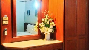 Quarto de hotel com uma toucador de madeira, um espelho, um vaso com flores, uma cama e um cesto de lixo.