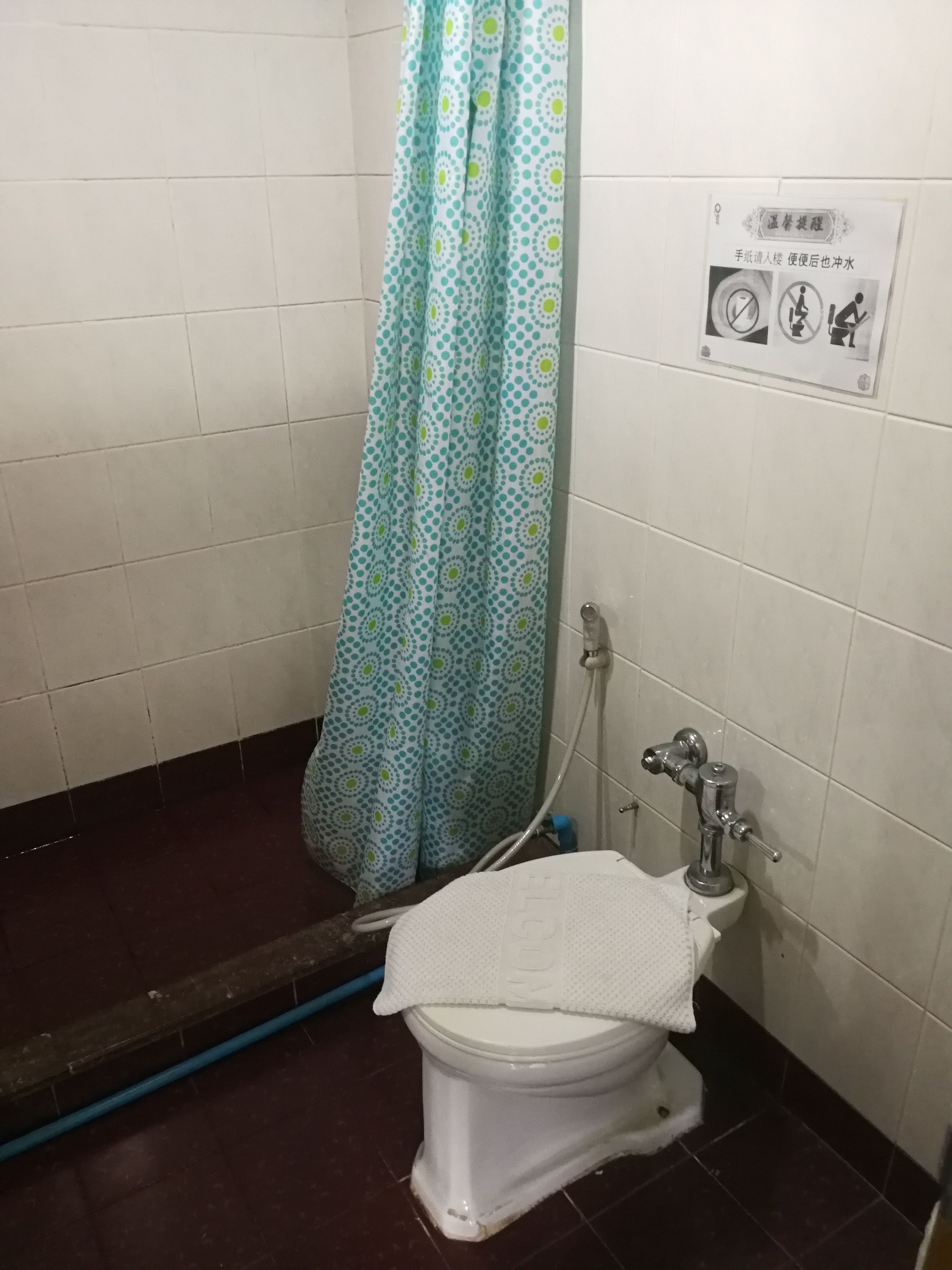 A small bathroom with a toilet, a shower curtain, and a hand-drawn sign on the wall.