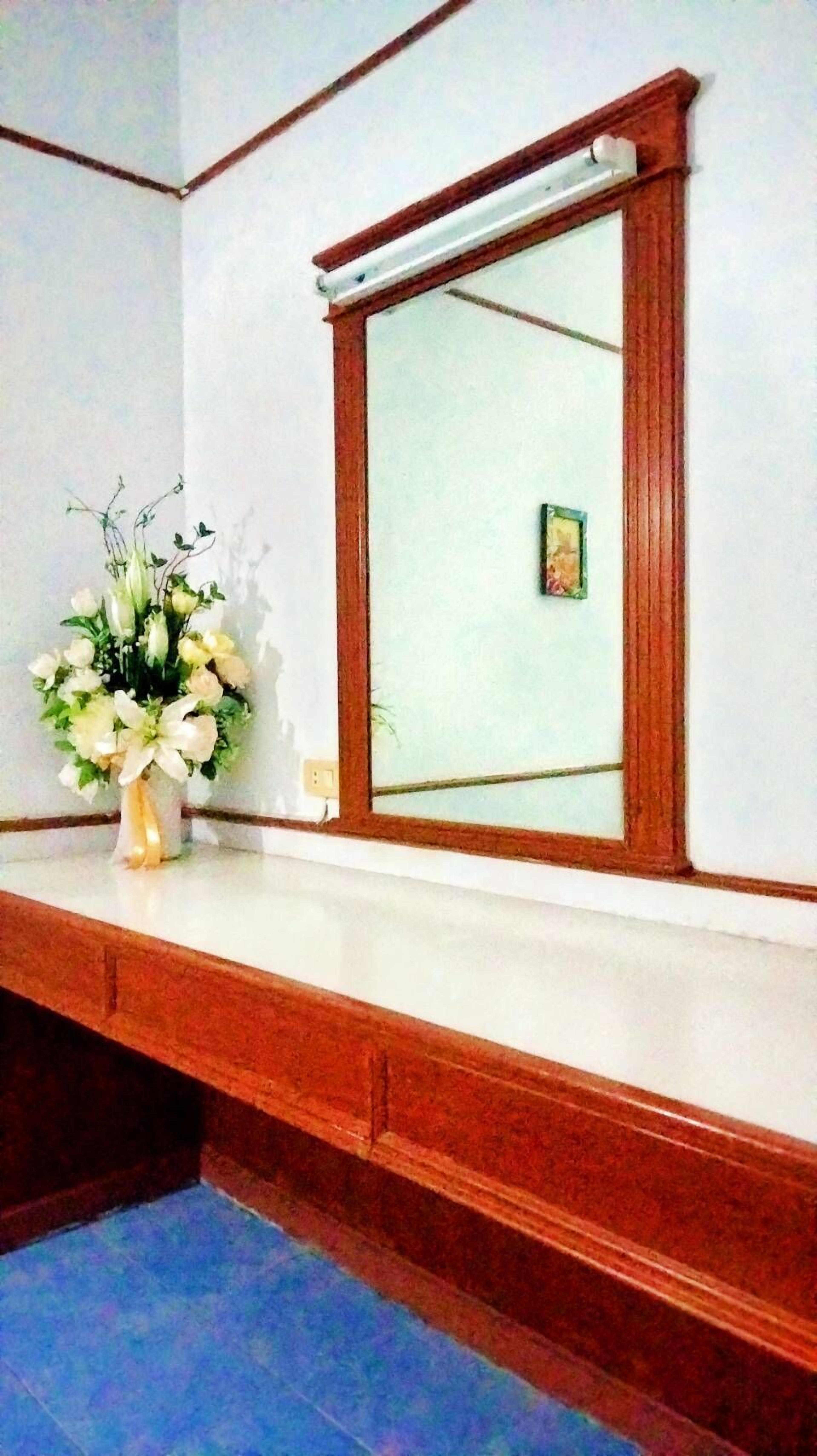 Una habitación con un espejo de marco de madera, un florero blanco con flores y un suelo de baldosas azules.
