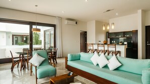 Una sala de estar moderna con un sofá color turquesa, sillas de madera, una mesa de centro y un comedor con una mesa y sillas.