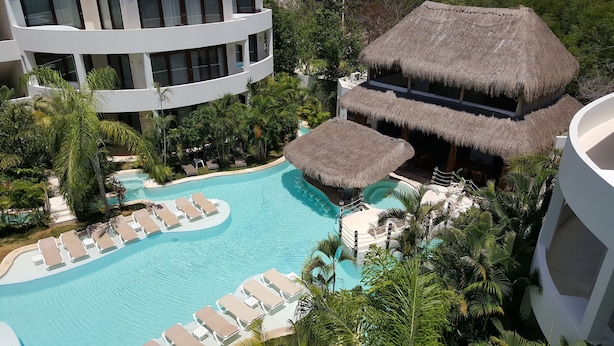 Un resort con piscina, sillas de descanso y construcciones de techo de paja.
