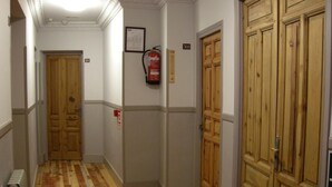 Un couloir avec des portes en bois, un extincteur et un radiateur.