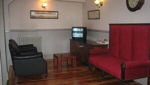 Un salon doté d’un plancher en bois, d’un fauteuil rouge, d’un canapé noir, d’une table basse en bois, d’un téléviseur posé sur un meuble en bois et de deux appliques murales.