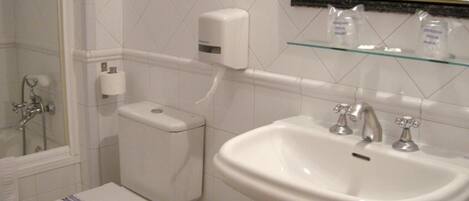 A bathroom with a toilet, sink, and a glass shelf above the sink.