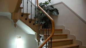 Un escalier en bois avec une rampe courbée et un pot de fleurs placé en haut.