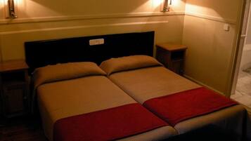 A double bed with two pillows and a red blanket, bedside tables with lamps, and a wall-mounted light fixture.