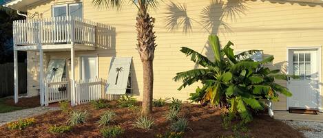 A two-story house with a balcony, a palm tree, and a banana plant in the front yard.