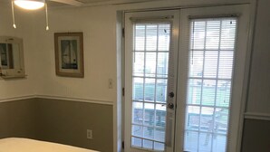 Un dormitorio con cama, ventilador de techo, puerta con persianas y vistas al exterior.