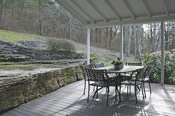 A covered patio with a table and chairs, stone wall, and forest view. - Wooded Cottage near Downtown Franklin & Leiper's Fork! (Franklin)