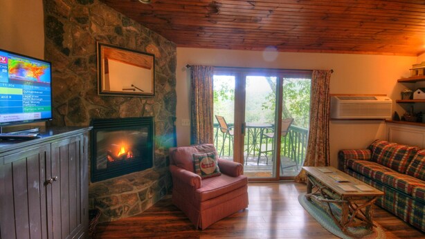A cozy living room with a stone fireplace, a television, a sofa, and a balcony with outdoor seating. - Vacation Cottage in Premier Resort (Boone)