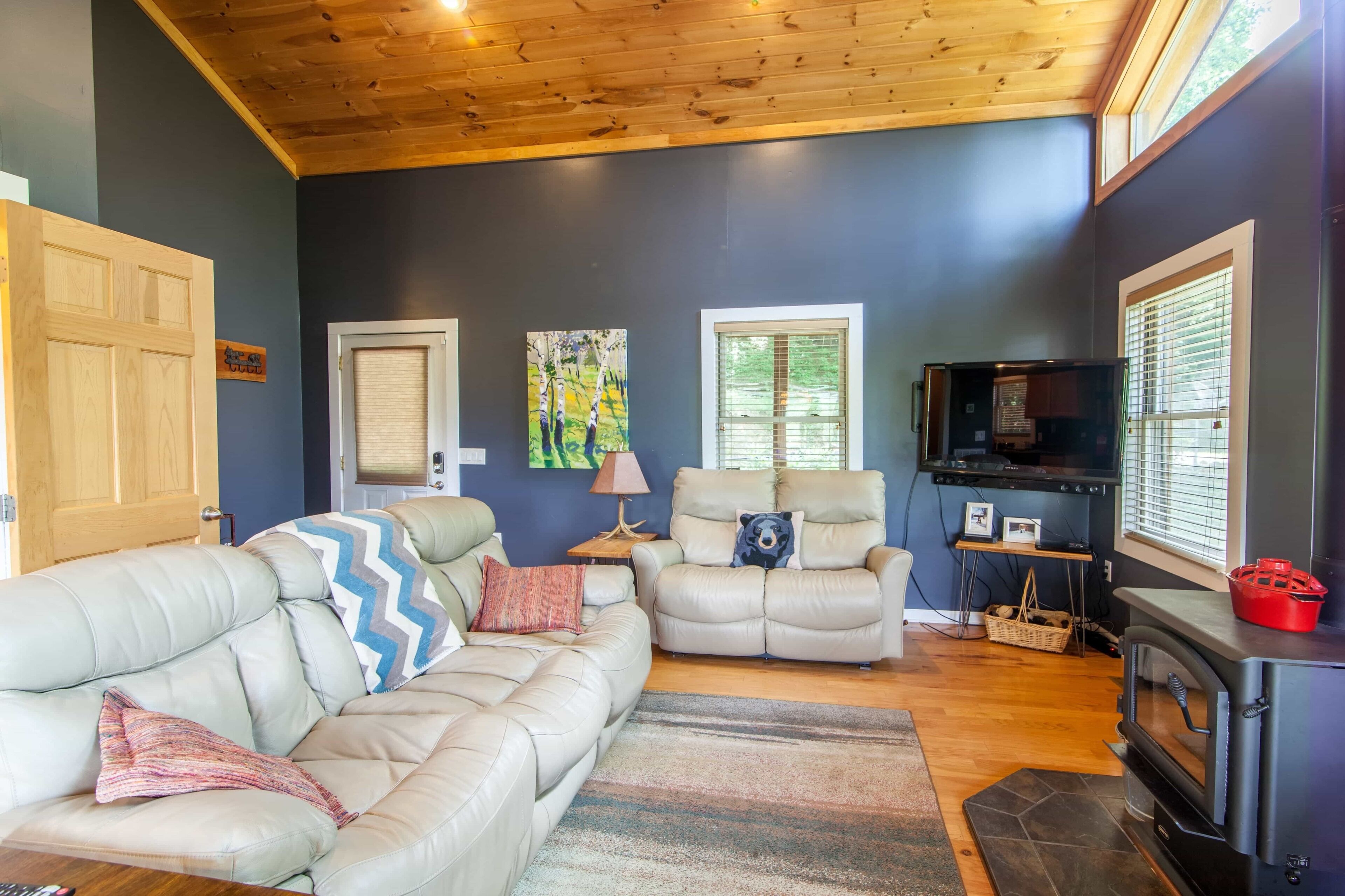 A living room with a fireplace, two sofas, a television, and a wooden ceiling.