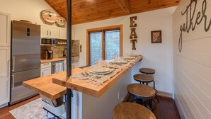 Una cocina con una mesa de madera larga lista para comer, un refrigerador y una ventana con persianas.