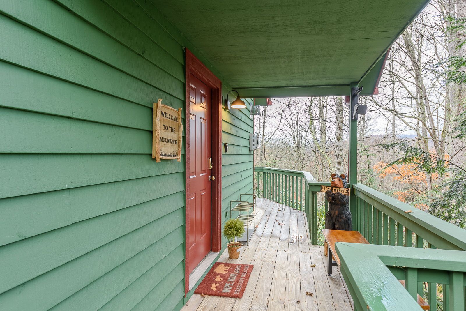 A green wooden building with a red door and a welcome sign.