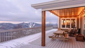 A wooden deck with a table and chairs, overlooking a snowy landscape with mountains in the background. - Mountain View Lodge on Seven Devils (Seven Devils)