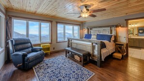 A cozy room with a bed, a leather chair, a bench, and a view of the mountains through large windows. - Mountain View Lodge on Seven Devils (Seven Devils)