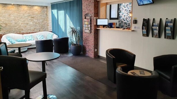 A modern hotel lobby with a sofa, round tables, and a reception desk. - Les Pelouses (Cucq)