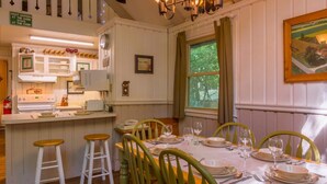 A dining area with a table set for four, wooden chairs, a kitchen in the background, and a painting on the wall. - Peaceful Chalet Close to Skiing (Beech Mountain)