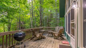 A wooden deck with Adirondack chairs, a grill, and a view of a forest. - Peaceful Chalet Close to Skiing (Beech Mountain)