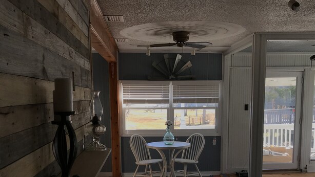 A room with a wooden wall, a ceiling fan, a table with two chairs, and a window with blinds. - The Buccaneer-Cottage, great for a couple or small family. (Ocracoke)