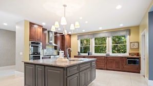 A spacious kitchen with a large island, dark cabinetry, and a modern chandelier. - Luxury Home with In-law Apartment (Boone)