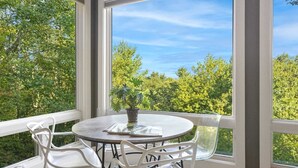 A round table with chairs and a potted plant, set against a backdrop of trees and a clear sky through large windows. - Luxury Home with In-law Apartment (Boone)