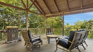 An outdoor covered patio with a grill, two chairs, and a table. - Luxury Home with In-law Apartment (Boone)