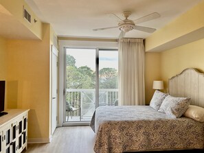 A hotel room with a bed, a ceiling fan, a balcony with a chair, and a TV on a cabinet. - Spectacular view, Big corner balcony, Lagoon pool, Baytowne & free shuttle (Miramar Beach)