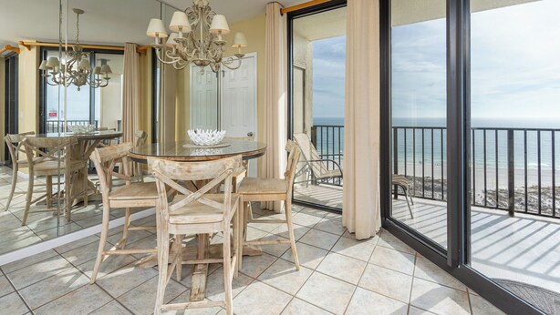 A dining area with a round table and chairs, a chandelier, and a view of the ocean through large sliding doors.