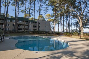 A swimming pool surrounded by trees, with a multi-story building in the background.