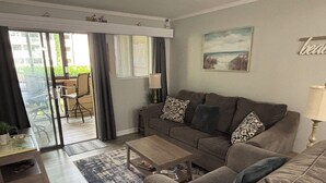 Un salon comprenant un canapé, une table basse et une porte vitrée donnant sur un espace extérieur aménagé avec une chaise et une table.