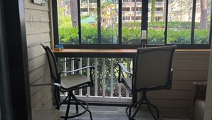 Une véranda avec deux chaises, une table en bois et une vue sur un quartier résidentiel, avec des arbres et des immeubles.