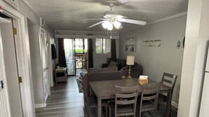 Un coin repas avec une table et des chaises en bois, un ventilateur de plafond et une vue sur l’extérieur grâce à une porte coulissante.