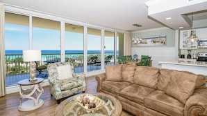 A living room with a large window, a brown sofa, a patterned armchair, a glass coffee table, and a small side table.