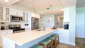 A kitchen with white cabinets, a large island with bar stools, stainless steel appliances, and pendant lighting.